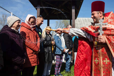 GORENKA, KYIV REG, UKRAINE - Apr. 24, 2022: People attend an Orthodox Easter church service and orthodox priest sprays holy water on believers and baskets in Gorenka, Kyiv region, Ukraineのeditorial素材