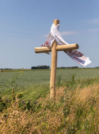 CHERNIHIV REG, UKRAINE - Jun. 19, 2022: War in Ukraine. A grave wooden cross with an embroidered towel on the side of the road along a wheat field. Landscapes of Ukraine after the Russian invasionのeditorial素材