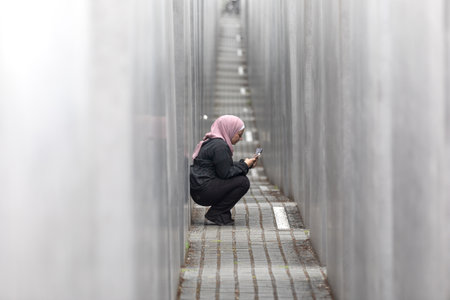 BERLIN, GERMANY - Jun. 28, 2022: A young woman in a hijab with a mobile phone inspects and photographs the Holocaust memorial in Berlinのeditorial素材