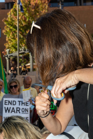 PORTLAND, OREGON, USA - Oct 15, 2022: People participate in a demonstration in solidarity with Iranian women and in memory of Mahsa Amini killed by the Iranian police. A woman cutting off her hair.のeditorial素材