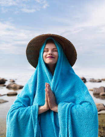 A youngA young girl with a Vietnamese straw hat and a blue cape on the seashoreの写真素材