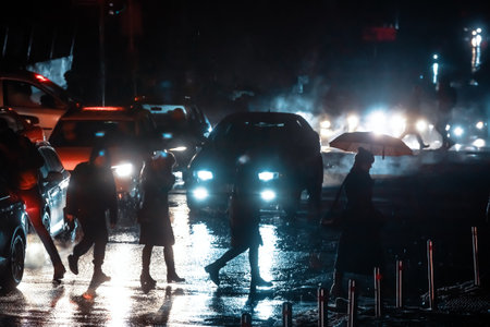 KYIV, UKRAINE - Dec. 16, 2022: Passers-by cross the street at a pedestrian crossing illuminated by car headlights. Dark buildings without light during a blackout in Kyiv.のeditorial素材
