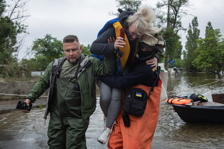 KHERSON, UKRAINE - Jun. 12, 2023: Rescue workers and volunteers can be seen carrying local people out of the flooded area on their handsのeditorial素材
