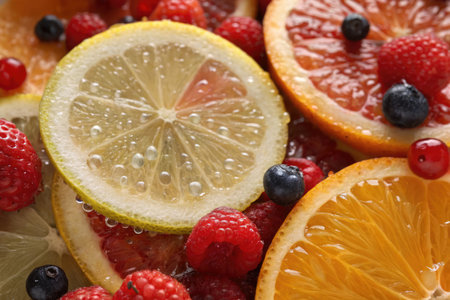 Slices of fresh oranges and lemons are surrounded by colorful berries, creating an enticing arrangement. Bubbles add a refreshing touch to this vibrant fruit mix.の写真素材