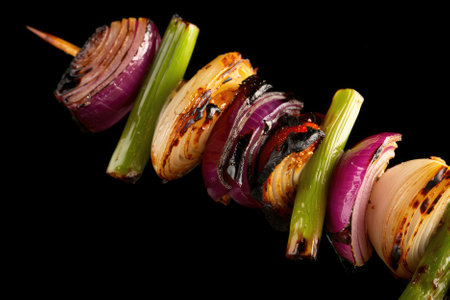 Assorted vegetables including purple and green onions are skewered and grilled to perfection. The vibrant colors and charred edges highlight the preparation of a delicious outdoor dish.の写真素材