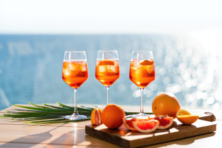 Three vibrant cocktails with ice and citrus slices are displayed on a wooden table overlooking the sparkling ocean. Fresh fruit adds to the tropical atmosphere, perfect for relaxation.の写真素材