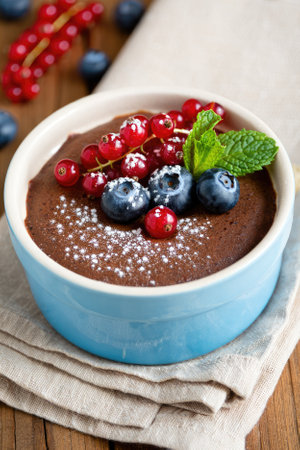 A joyful family dessert made of rich chocolate and topped with blueberries and red currants, garnished with a mint leaf. Perfectly served in a light blue dish on a wooden table.の写真素材