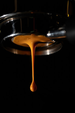 Dark liquid cascades down from a coffee machine, creating a rich stream on a shiny surface. The atmosphere is cozy as the aroma of fresh coffee fills the air in the bustling cafe.の写真素材