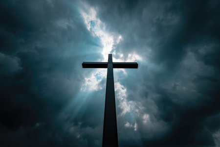 A large cross stands tall against a backdrop of dark clouds and bright rays of light. The contrast creates a powerful atmosphere, evoking feelings of hope and faith in a dramatic landscape.の写真素材