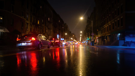 A rainy night scene in a city with cars driving on wet asphalt, reflecting lights and buildings.