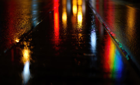 The pavement glistens with reflections of vibrant lights during a rainy night, creating a beautiful...