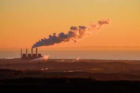 An industrial plant spews smoke into the orange-hued sky during sunset, highlighting environmental concerns. The smoke plume drifts gracefully.の写真素材