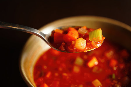 Close up of a spoon filled with vegetable soup held above a bowl.の写真素材