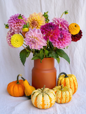 A vibrant still life featuring a terracotta vase brimming with colorful dahlias, complemented by an array of gourds. A cheerful composition.の写真素材