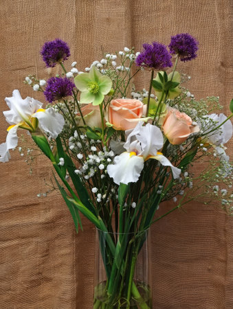 A beautiful floral arrangement in a glass vase, featuring irises, roses, and other flowers against a neutral background.の写真素材