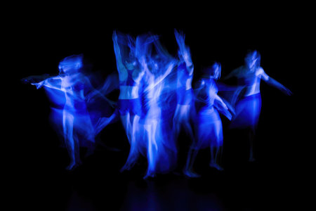 A group of dancers, blurred by motion, create a striking blue light effect against a dark background, emphasizing movement and energy.の写真素材