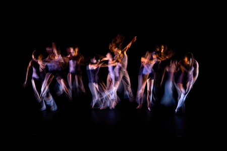 A blurred shot captures dancers in motion, their bodies blending and stretching across the frame against a stark black background.の写真素材