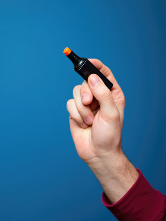 A person's hand holding a black marker with an orange tip against a blue background.の写真素材