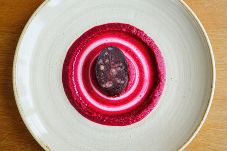 A close up shot of a slice of blood sausage with beetroot puree, artfully presented on a white plate. The plate is set on a wooden surface.の写真素材