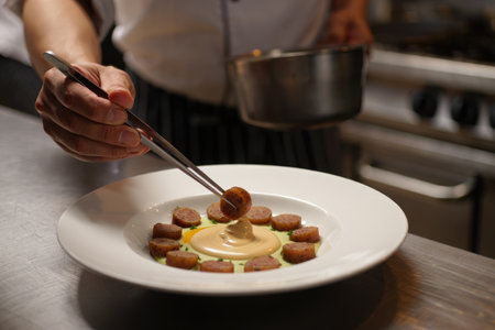 A chef delicately places a sausage on a beautifully plated dish with tweezers. The scene highlights fine dining and culinary expertise.の写真素材