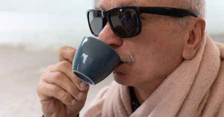 An older man wearing sunglasses sips from a mug, enjoying his drink.