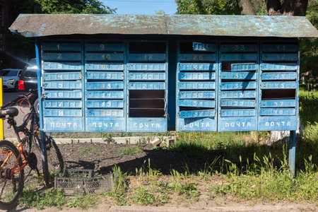 An old, blue, weathered post office box with multiple compartments, with a bicycle parked nearby, set against a backdrop of greenery and a sunny day.の写真素材