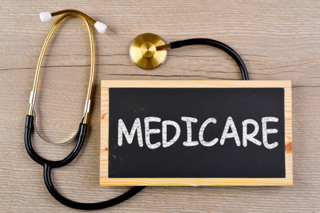 A stethoscope rests beside a chalkboard with the word medicare written on it, set against a wooden background.の写真素材