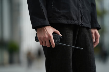 A person in a black jacket and pants holds a walkie talkie, possibly a security guard. Close up shot.の写真素材