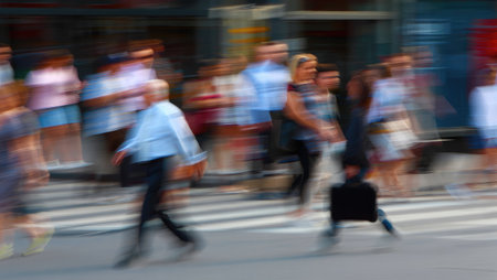 People are captured in a blur as they move across a crosswalk, creating a sense of movement and energyの写真素材