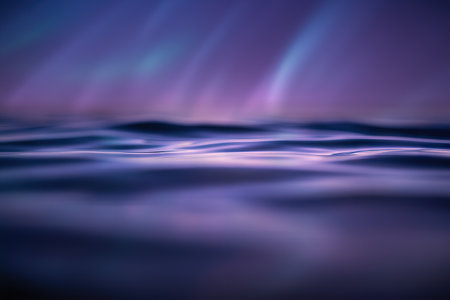Abstract background. Rippling water surface displaying gentle waves and subtle undulations. Soft, diffused purple and blue light reflects on the liquid, creating a serene and ethereal visual effect.の写真素材