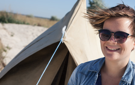 Portrait of young smiling woman with sunglasses near the tent on a sandy beachの写真素材