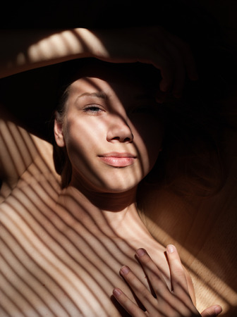 Close up portait of beautiful girl wearing bra. Sunlight through jalousie shines on beautiful woman's face.の写真素材