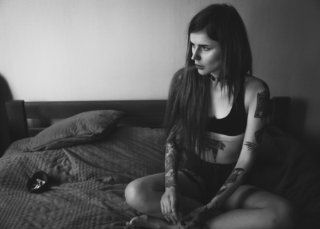 Young tattooed woman with long hair smoking in bedroom, wearing black top and choker, sitting on bed. black and white portraitの写真素材