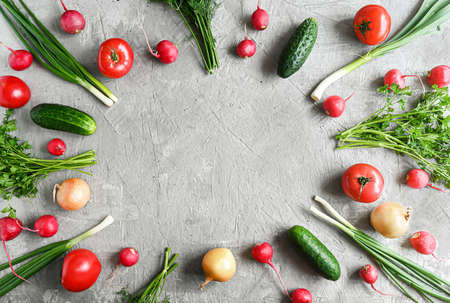Whole fresh healthy vegetables: tomatoes, cucumbers, radishes, onions and herbs on a light gray...
