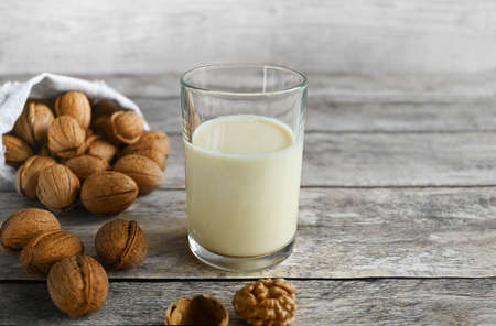 Vegan walnut milk in a glass and organic walnuts in a linen bag on a natural wooden table, non-dairy...