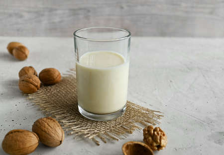 Vegan walnut milk in a glass and organic walnuts on a natural table, non-dairy alternative milk,...