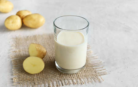 Vegan potato milk in a glass and potatoes on burlap on the wooden background, non-dairy alternative milk, copy space. Potato milk contains many useful vitamins and minerals: vitamin B6, vitamin C, potassium, silicon, cobalt, copper, molybdenum, chromium.の写真素材