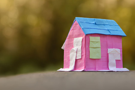 Paper house on a wooden table with bokeh background, close up