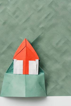 Origami paper house on green background, top view, copy space