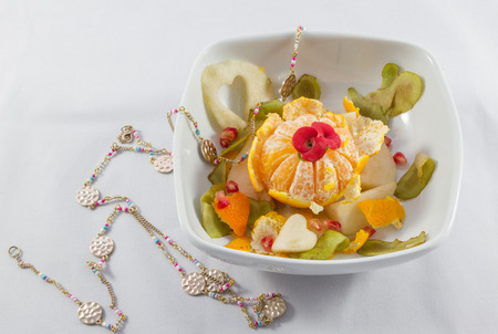 Decorated fruit salad bowl and necklace compositiom on a white backgroundの写真素材