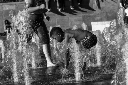 Manchester, United Kingdom - 15 August, 2017: Children playing at Picadilly Gardens water fountains in Manchester city center on a sunny summer afternoon- photo in black and whiteのeditorial素材