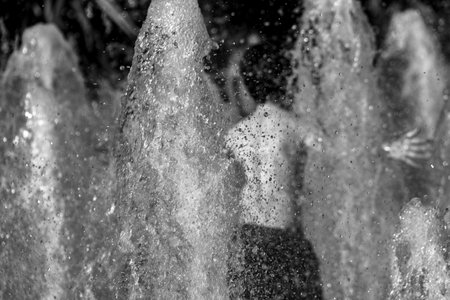 Manchester, United Kingdom - 15 August, 2017: Child playing at Picadilly Gardens water fountains in Manchester city center on a sunny summer afternoon- photo in black and white, rear viewのeditorial素材