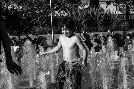 Manchester, United Kingdom - 15 August, 2017: Child playing at Picadilly Gardens water fountains in Manchester city center on a sunny summer afternoon- photo in black and whiteのeditorial素材