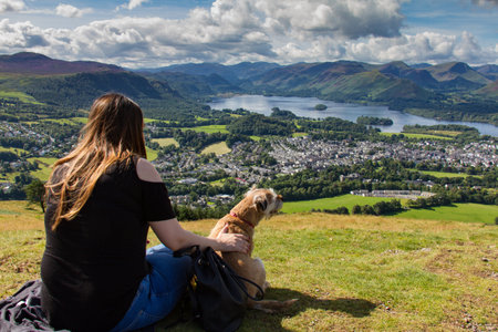 Keswick, United Kingdom - 13 August, 2017: Girl touching dog and gazing at Keswick and lake Derwent Water from Latrigg, Cumbria, UKのeditorial素材