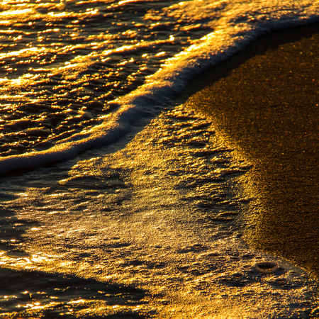 Close-up of abstract colorful shapes created by breaking waves on a sandy shore and sun reflections at sunsetの写真素材