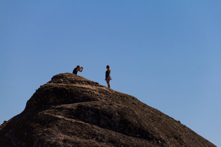 Meteora, Greece - 9 October, 2017: A man takes aphoto of a girl using a smartphone on top of a rock at Meteora monastery complex in Greece