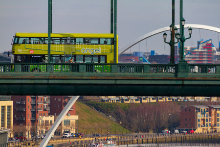 Newcastle, England - March 7, 2018: Green Double Decker bus crossing the Tyne Bridge and Millennium Bridge in the distance at Newcastle Quayside on a cloudy dayのeditorial素材