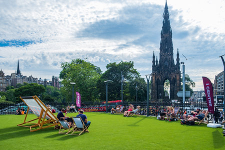 Edinburgh, United Kingdom - July 27, 2018: People enjoying the sun on lounge chairs near Scott Monument on Princes Street in Edinburgh on a hot summer afternoonのeditorial素材