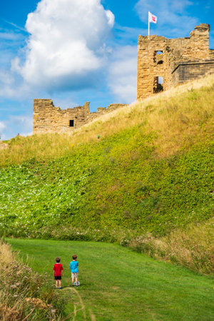 Tynemouth, England - August 2, 2018: Two boys with a football gaze towards Tynemouth Priory and Castle.のeditorial素材