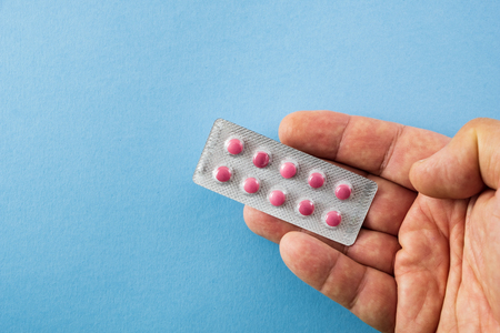 Diagonally arranged hand holding a blister pack of pink pills on blue background with copyspace- healthcare and medical conceptの写真素材